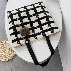 Detail of checkered canvas tote bag with brown plush bear charm and sturdy shoulder strap