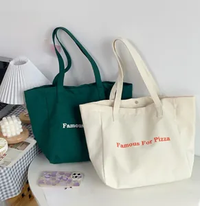 Détail de sacs cabas en toile vert et crème avec imprimé Famous For Pizza