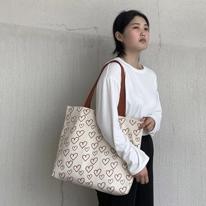 Detailed view of cream canvas tote bag with red heart pattern and wide brown strap