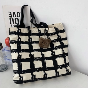 Close-up of black and white checkered canvas tote bag with a cute brown plush bear charm
