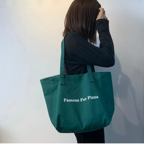 Détail d'un cabas en toile vert foncé avec texte Famous For Pizza porté par un mannequin
