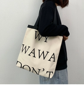 Detail of off-white canvas tote bag with black straps and bold letter print on side