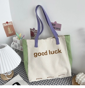 Detail of color-block canvas tote bag with good luck print and purple handle on desk