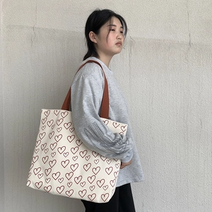 Detail of canvas tote bag with red heart patterns and wide brown shoulder straps