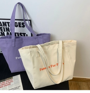 Gros plan de grands sacs cabas en toile violet et blanc cassé avec texte 'Famous For Pizza'