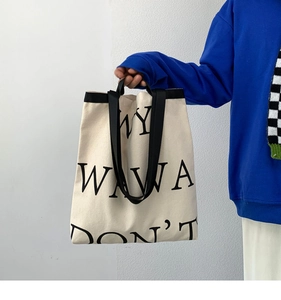 Detail of canvas tote bag with black letter print and contrast handles worn with blue hoodie