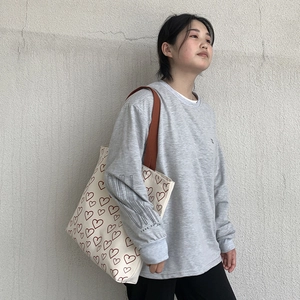 Detail of a large canvas tote bag with red heart prints and dark brown shoulder straps