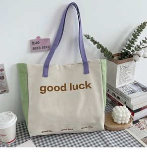 Detail view of canvas tote bag with color blocking design and good luck slogan on table
