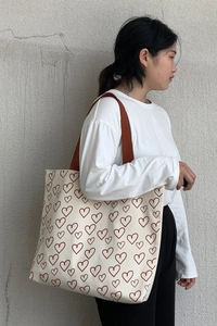 Close-up of minimalist canvas tote with red heart pattern and brown shoulder strap