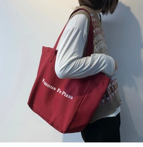 Grand sac cabas en toile rouge avec imprimé Famous For Pizza porté par un modèle