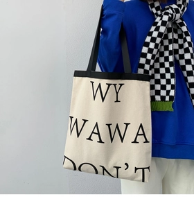 Detail of canvas tote bag featuring bold black letter printing and durable shoulder straps