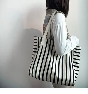 Side view of large black and white striped canvas tote bag on female model shoulder