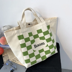 Detail of canvas tote bag featuring green checkerboard pocket and 'Boom' printed text