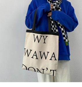 Detail of a beige canvas tote bag with bold black typography on a casual outfit