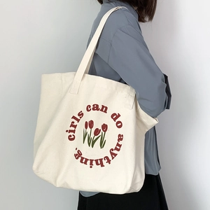 Detail of canvas tote bag with tulip print and girls can do anything slogan on model