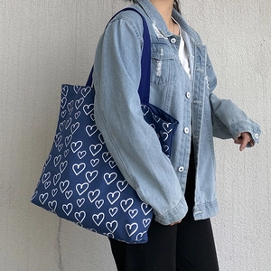 Detail of navy canvas tote bag with white heart print and wide shoulder strap on model