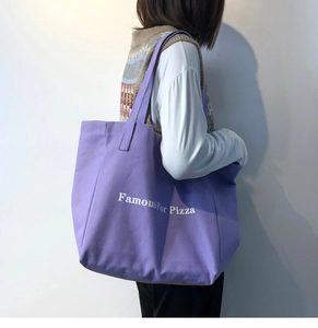Sac fourre-tout en toile violette avec imprimé Famous For Pizza porté à l'épaule au quotidien