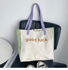 Detail of color-block canvas tote bag with good luck print on black leather chair