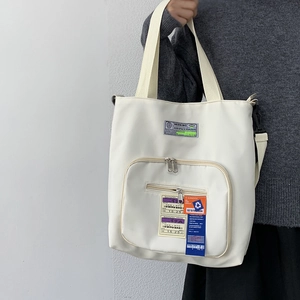 Detailansicht der cremeweißen Nylon-Tragetasche mit vielen Taschen und Dekoschildern