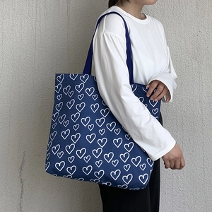 Navy blue canvas tote bag with white heart print shown on model for a casual look