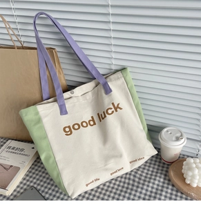 Detail of color-block canvas tote bag featuring Good Luck text and purple woven handles