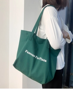 Détail du sac cabas en toile vert foncé avec lettrage blanc porté par un mannequin