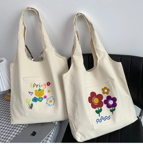 Close-up of cream canvas tote bags with bear and flower patterns and wide shoulder straps