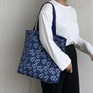 Blue canvas tote bag with white heart pattern worn by a model against a neutral wall