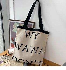 Detail of a beige canvas tote bag featuring black letter print on a wooden bench