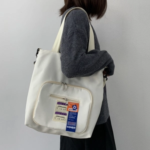 Detail der weißen Nylon-Tragetasche mit Bordkarten-Patch und orangefarbenem Etikett