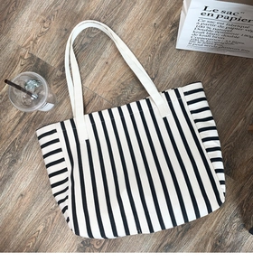 Close-up of black and white striped canvas tote bag on dark wooden floor with accessories