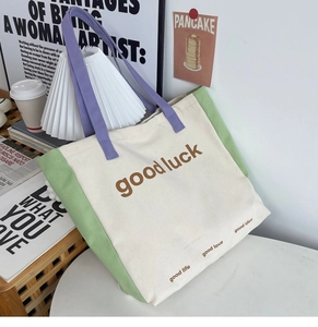 Detail of color-block canvas tote bag with purple straps and good luck typography