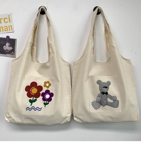Detail of off-white canvas tote bags with teddy bear and floral prints on front pockets