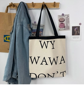 Detail of cream canvas tote bag with black typography hanging on a wooden hook