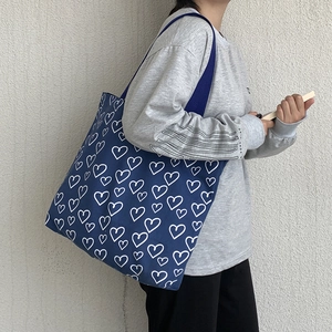 Detail of navy blue canvas tote bag featuring white hand-drawn heart patterns on a model