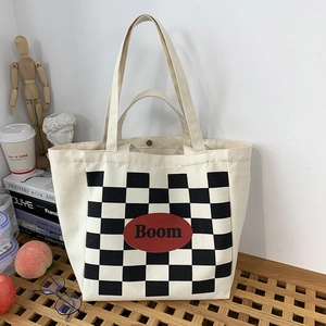 Detail of canvas tote bag featuring checkerboard print and Boom patch with snap closure