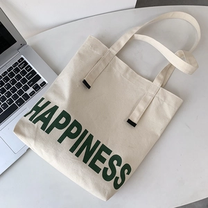 Vue détaillée du sac en toile crème avec texte Happiness vert sur un bureau