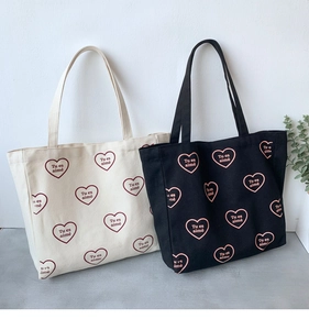 Détail de sacs fourre-tout en toile avec motifs de cœur et texte français 'Tu es aimé'