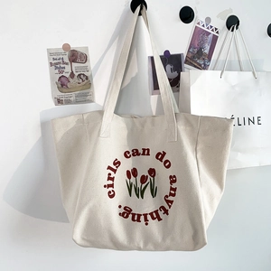 Close-up of canvas tote bag with red tulip print and 'girls can do anything' slogan
