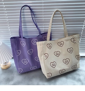 Détail de sacs cabas en toile violets et blancs avec motifs de cœurs et texte français