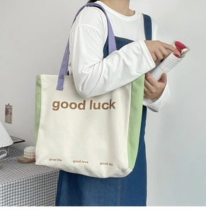 Detail of color-block canvas tote bag with good luck print and purple fabric handles