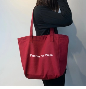 Détail d'un sac fourre-tout rouge en toile avec texte Famous For Pizza porté par un modèle