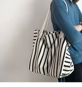 Detailed side view of large black and white striped canvas tote bag worn by a model