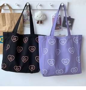 Détail de sacs fourre-tout en toile violette et noire avec motifs de cœurs et texte