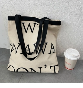 Close-up of minimalist canvas tote bag featuring black lettering and wide nylon strap