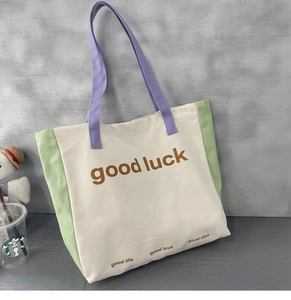 Detail of color-block canvas tote bag with good luck text and green side panels
