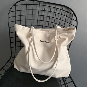 Minimalist off-white canvas tote bag with black lettering by morisot on a black chair