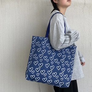 Detail of navy blue canvas tote bag featuring white hand-drawn heart patterns and wide strap