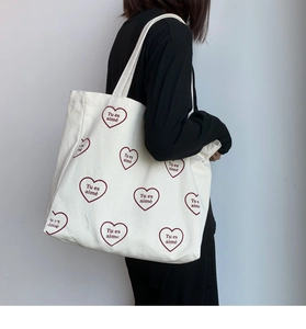 Détail d'un sac cabas en toile blanche avec des cœurs bordeaux et texte Tu es aimé