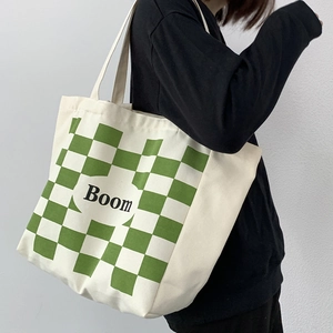 Detail of a large white canvas tote bag with green checkerboard pattern and Boom print